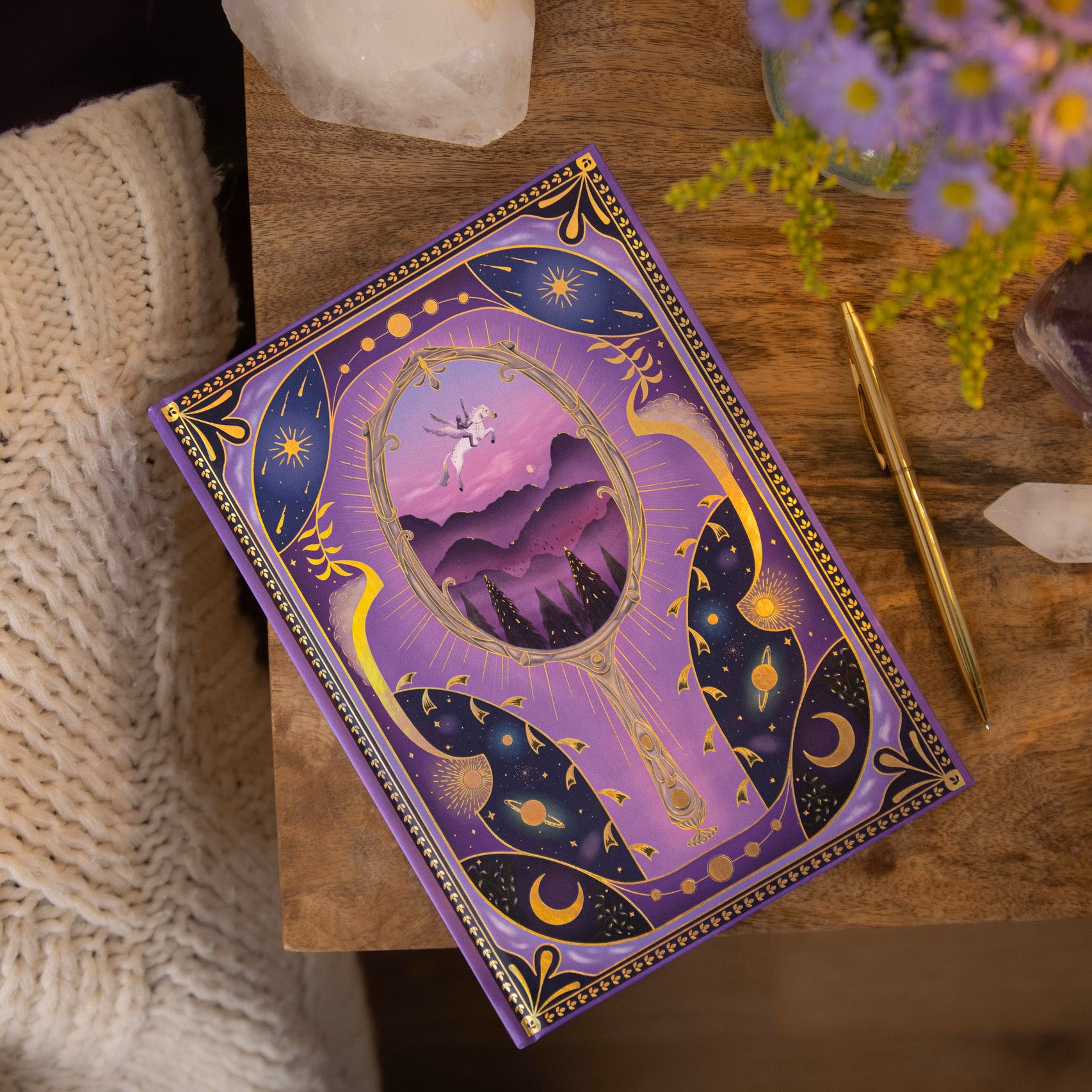 Decorative dream diary with purple and gold design on a wooden surface with flowers and crystals.