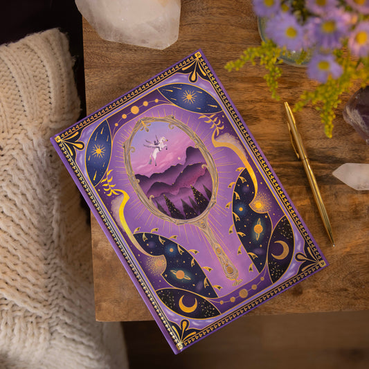 Decorative dream diary with purple and gold design on a wooden surface with flowers and crystals.