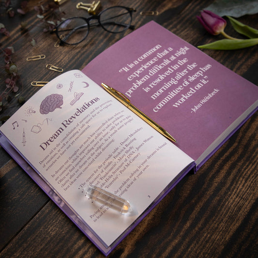 Open dream Journal with a purple cover on a wooden surface, featuring text and a pen.