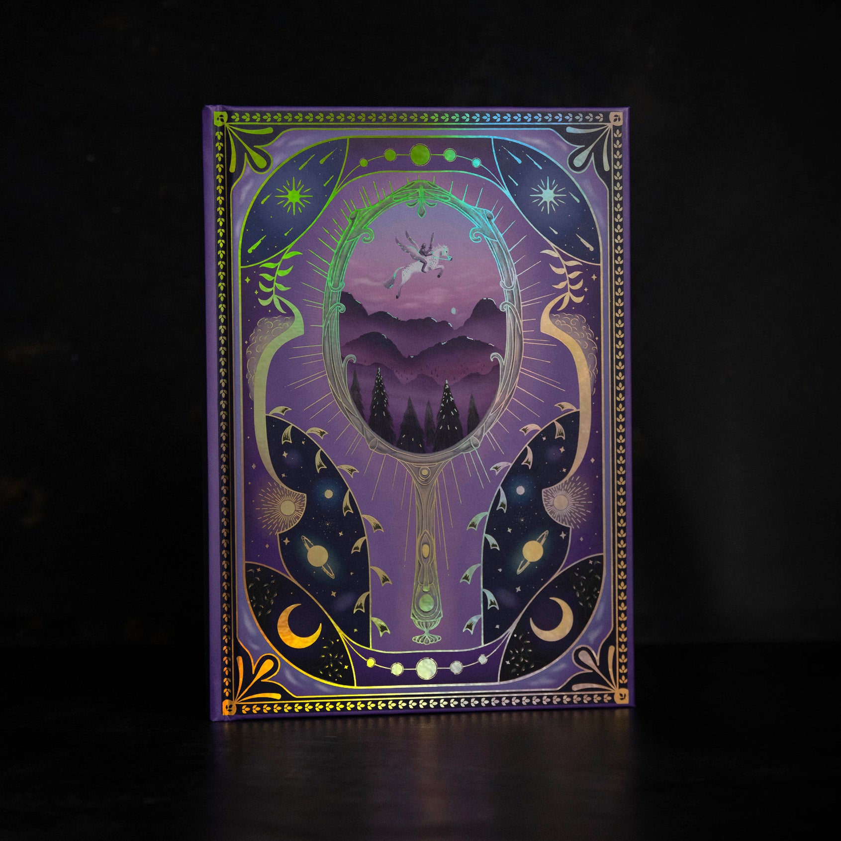Dream Journal on a black background showcasing its purple covering with gold leaf, stars, Moon, and a mirror. Seeing into a dream.